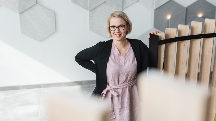 Henkilö seisoo Gradian aulatiloissa yläviistosta kuvattuna, katsoo hymyillen kameraan.